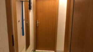 A narrow hallway with a wooden door, a green mat, and a trash bin.