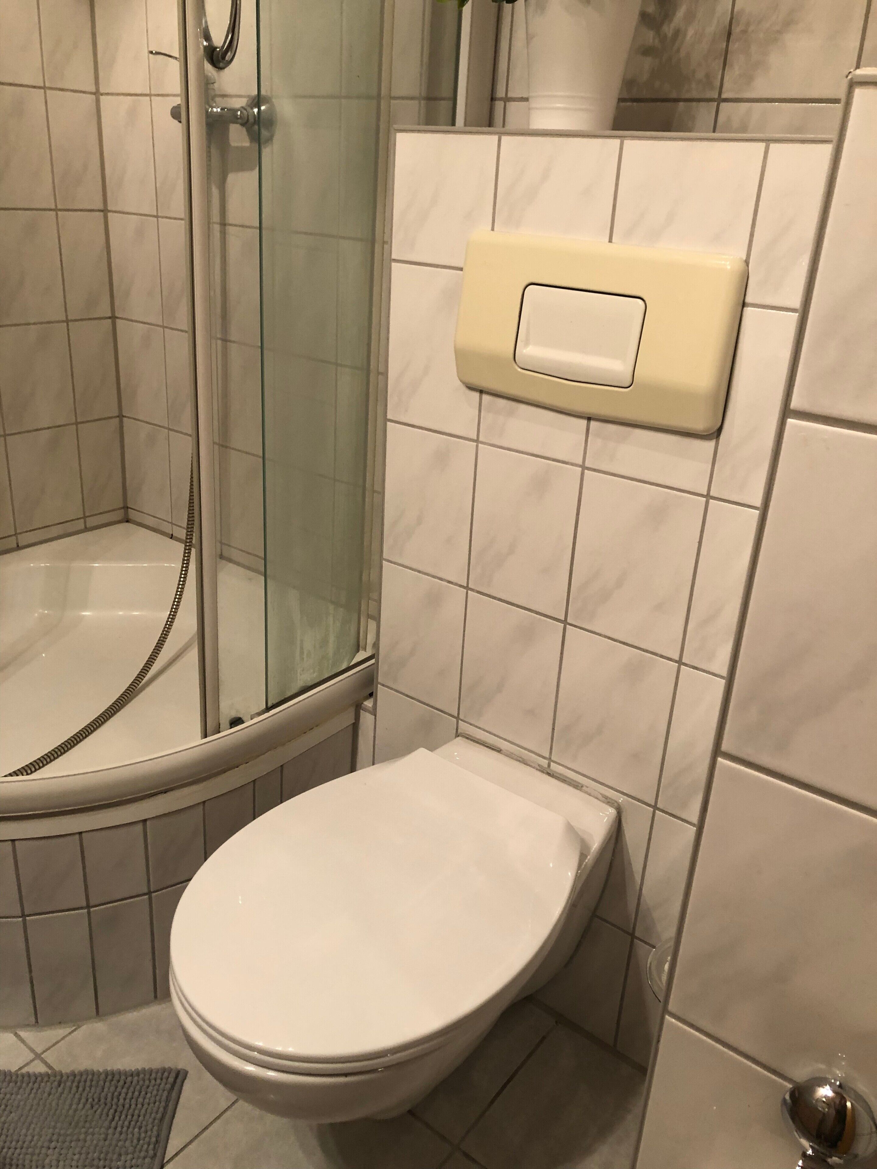 A bathroom with a glass-enclosed shower, a toilet, and a wall-mounted soap dispenser.