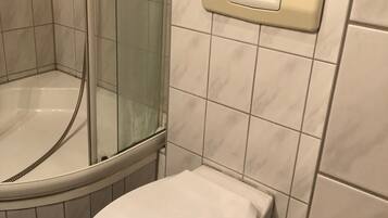 A bathroom with a glass-enclosed shower, a toilet, and a wall-mounted soap dispenser.