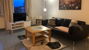 A living room with a TV, a sofa, a coffee table, a lamp, and a painting on the wall.