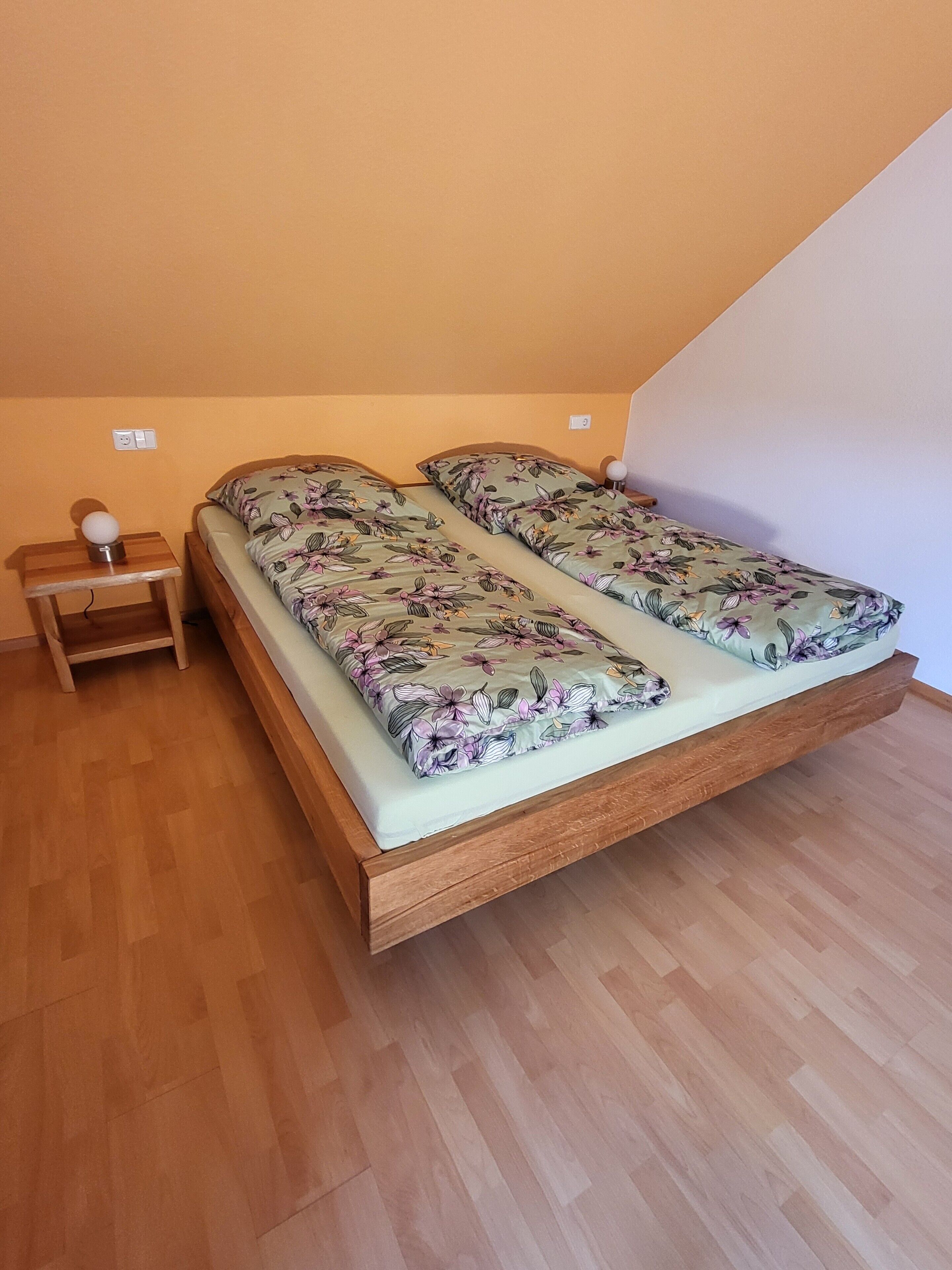 Una cama individual con colcha estampada en una habitación con suelo de madera y techo inclinado.