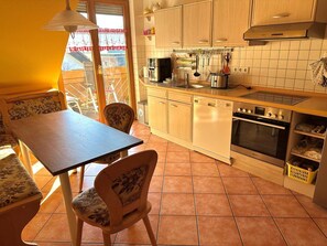Una cocina con armarios de madera, lavavajillas, horno y una zona de comedor con mesa y sillas.