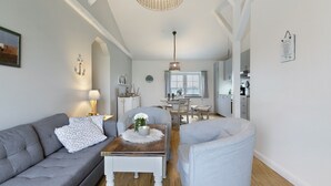 Una sala de estar moderna con un sofá, un sillón y una mesa de centro. En el fondo, hay una zona de comedor con una mesa y sillas.