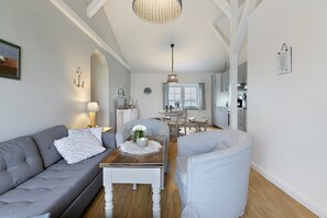 A modern living room with a sofa, armchair, and a coffee table. There is a dining area with a table and chairs in the background.