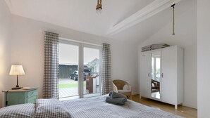 Un dormitorio con cama, mesita de noche, silla, armario y vistas al exterior.