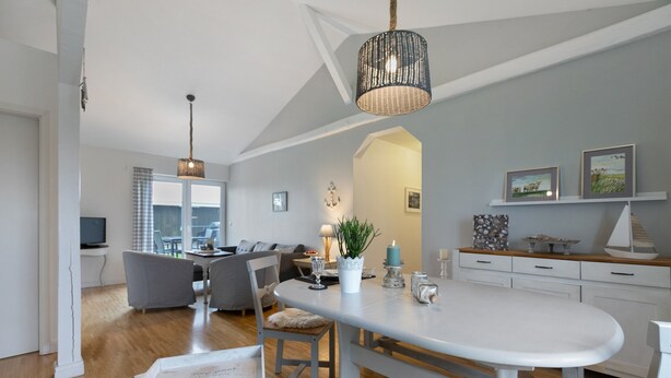 Una cocina moderna con una isla central, un comedor con mesa blanca y una sala de estar con sofá gris.