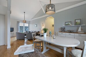 Una cocina moderna con una isla central, un comedor con mesa blanca y una sala de estar con sofá gris.