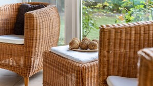 Wicker chairs with cushions, a small table with decorative items, and a view of greenery through a window. - Holiday Home 'Ferienhaus Sommerrose' with Private Terrace, Private Garden and Wi-Fi (Oberuckersee)
