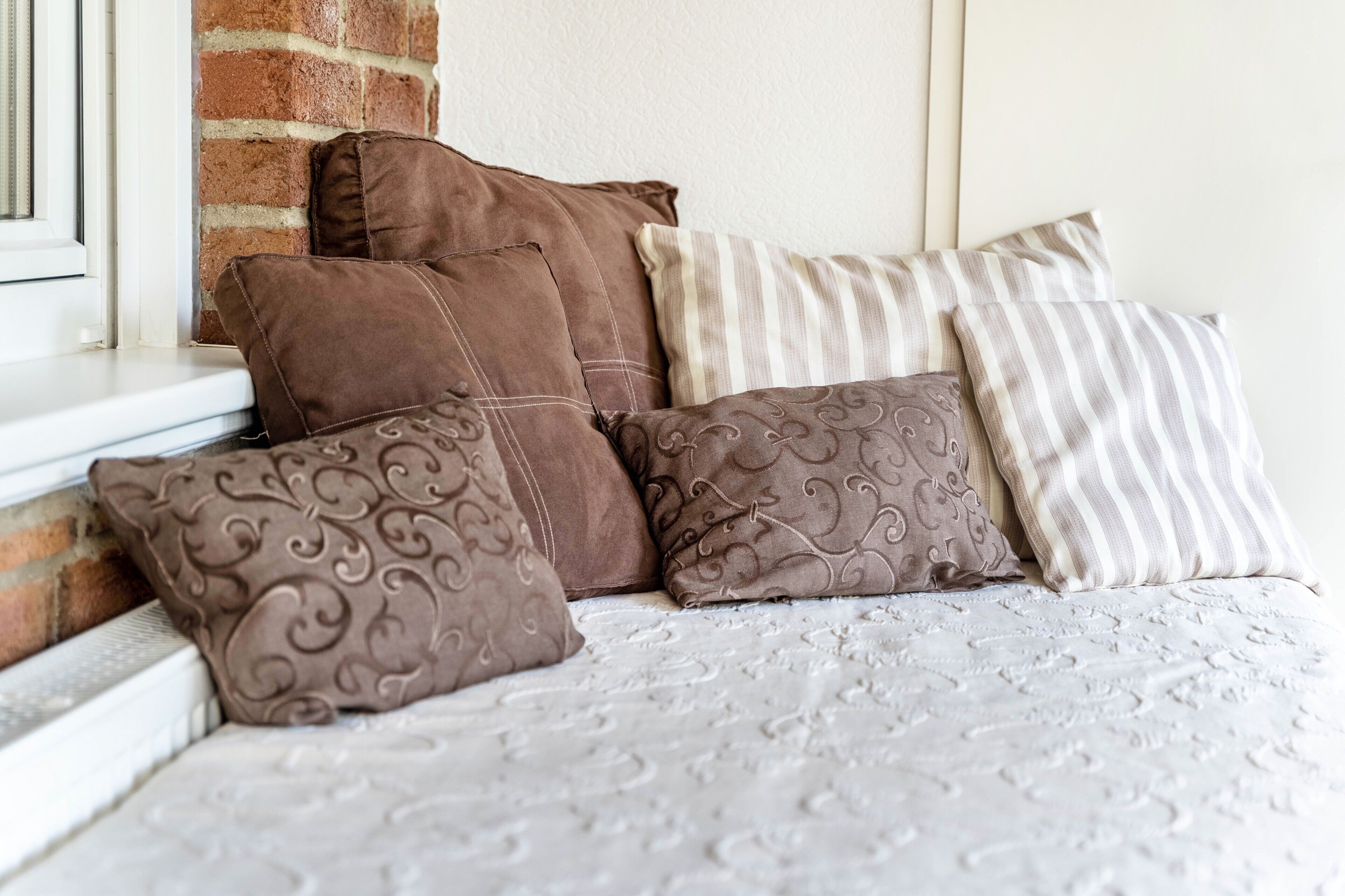 Una cama con una colcha blanca estampada y varias almohadas de diferentes texturas y diseños.