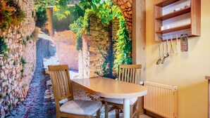 A dining area with a stone wall backdrop, a wooden table, two chairs, and a kitchen area with utensils hanging on the wall. - Holiday Home 'Ferienhaus Sommerrose' with Private Terrace, Private Garden and Wi-Fi (Oberuckersee)