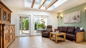 A living room with a sofa, armchair, and wooden coffee table. There is a large window with a view of greenery outside. - Holiday Home 'Ferienhaus Sommerrose' with Private Terrace, Private Garden and Wi-Fi (Oberuckersee)