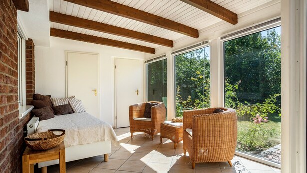 A bedroom with a bed, a wicker chair, a small table, and a large window. - Holiday Home 'Ferienhaus Sommerrose' with Private Terrace, Private Garden and Wi-Fi (Oberuckersee)