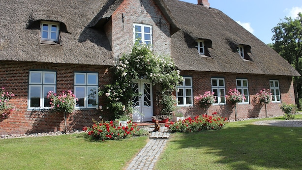 A traditional brick house with a thatched roof, a central door, and a small garden with flowers and a pathway.