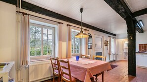 A dining area with a table set for four, wooden chairs, a hanging light fixture, and large windows with curtains.