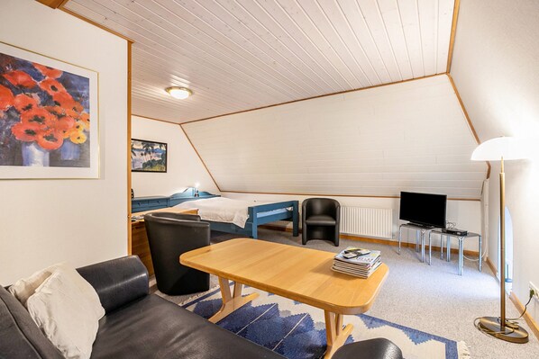 A cozy room with a bed, a desk, a chair, a sofa, a lamp, and artwork on the walls.