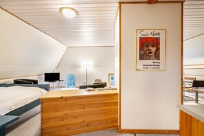 A room with a wooden desk, a bed, a television, and a framed picture on the wall.