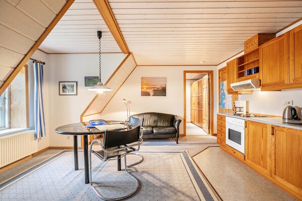 Une cuisine moderne avec des meubles en bois, un coin repas comprenant une table et des chaises, et une vue sur l’extérieur par une fenêtre.