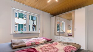 A bedroom with two beds, a large mirror, and a window with shutters. - Holiday Apartment 'Fewo unter der Kirche' with Wi-Fi (Herbolzheim)