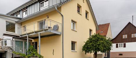 A two-story building with a balcony, a staircase, and a tree in front.