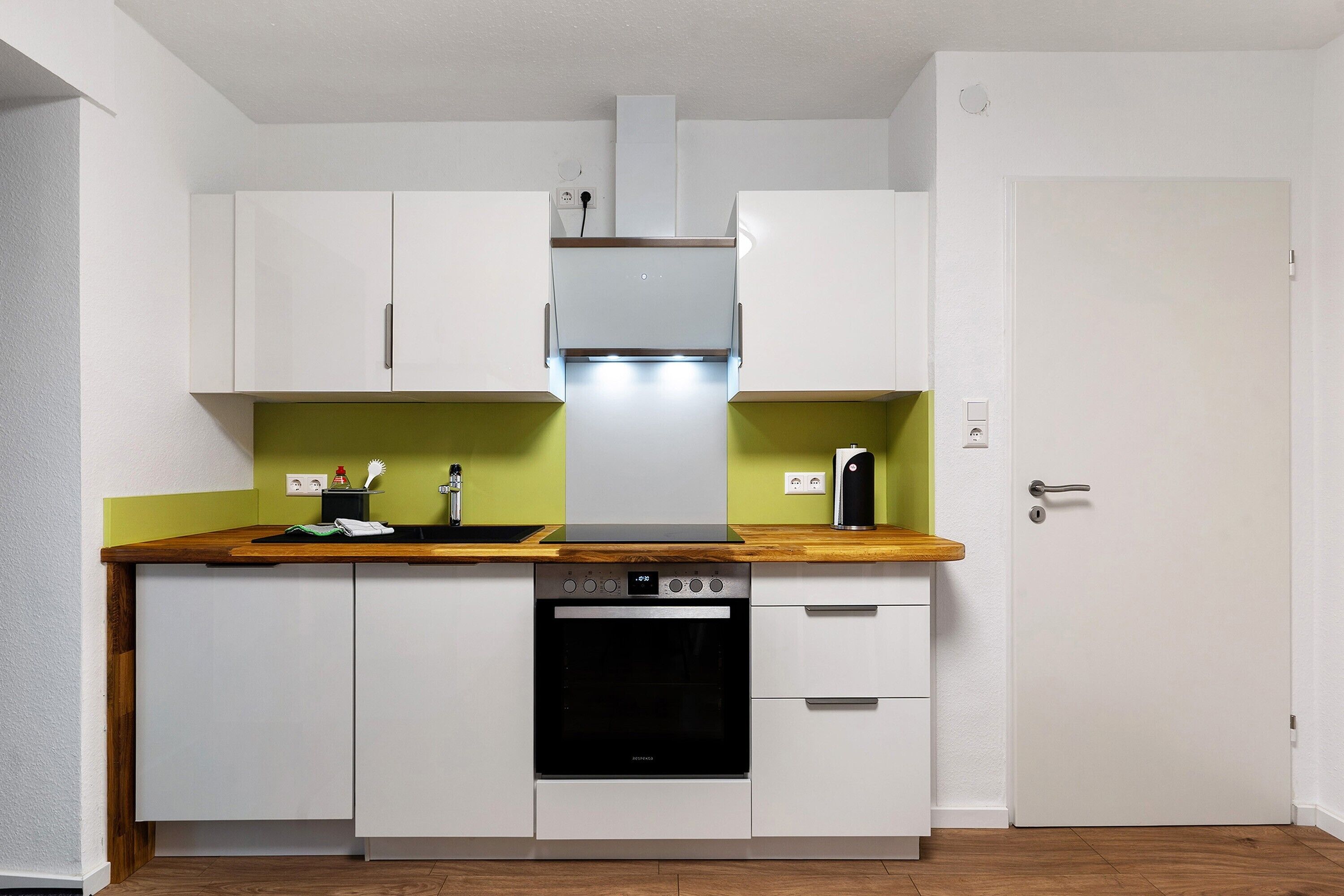 Une cuisine de taille réduite avec des meubles blancs, un four encastré et un plan de travail en bois.