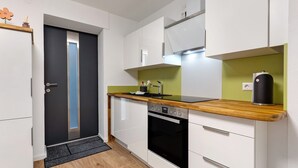 A modern kitchen with white cabinets, a wooden countertop, a built-in oven, and a green accent wall. - Holiday Apartment 'Fewo unter der Kirche' with Wi-Fi (Herbolzheim)