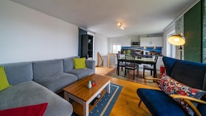 Una sala de estar moderna con un sofá, una mesa de centro y un sillón azul. Se observa un comedor con una mesa y sillas al fondo.