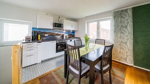 Cocina pequeña con armarios blancos, un microondas y una estufa. Hay una mesa de comedor con sillas y un florero con flores.