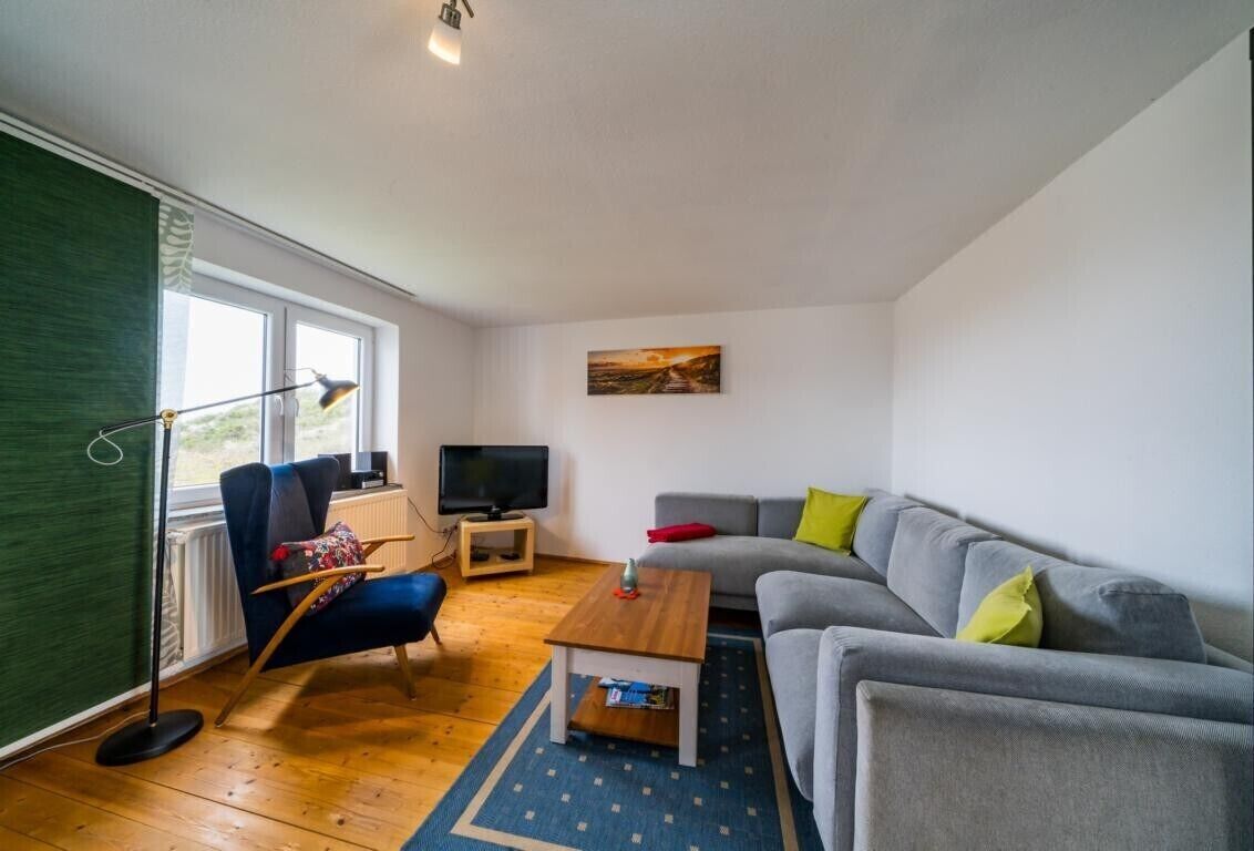Una sala de estar con sofá, sillón, mesa de centro, televisión y un cuadro en la pared.