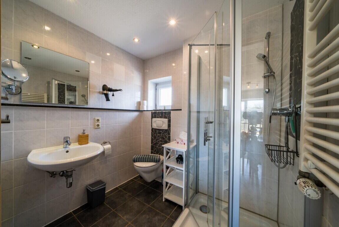 Ein modernes Badezimmer mit Duschkabine aus Glas, Waschbecken, Toilette und Spiegel.