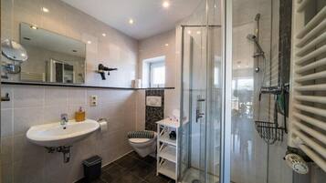 Ein modernes Badezimmer mit Duschkabine aus Glas, Waschbecken, Toilette und Spiegel.