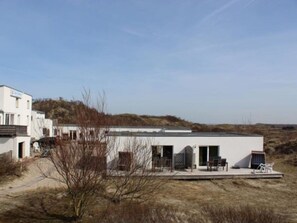 A modern building with a flat roof, a covered outdoor area with seating, and a view of the surrounding landscape.