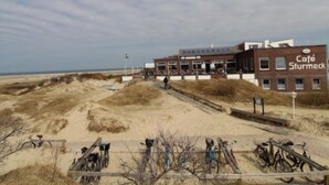 A building with a sign reading 'Café Sturmeck' on a sandy beach with bicycles parked in front.