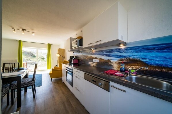 Une cuisine moderne dotée d’un grand îlot central, d’un four à micro-ondes encastré et offrant une vue sur l’océan grâce à une fresque murale.