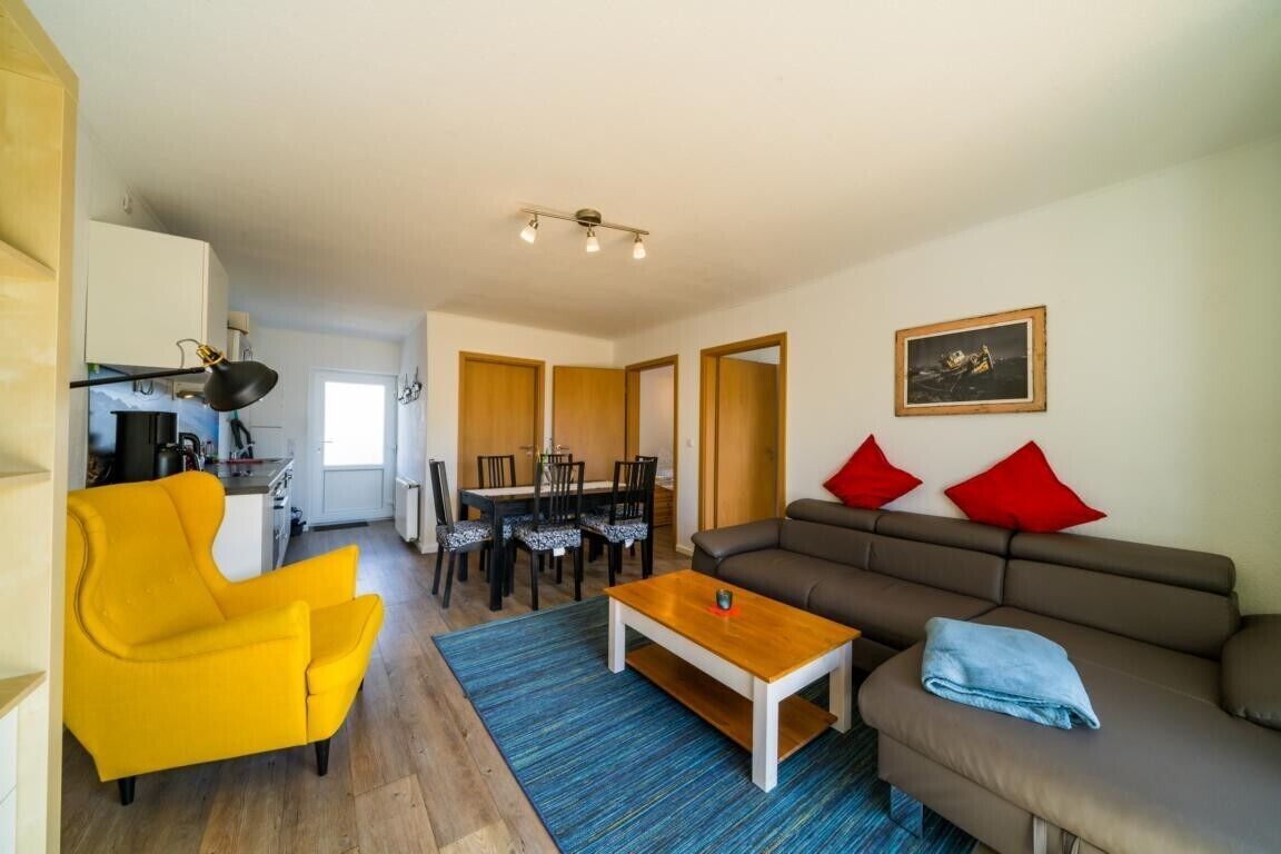 Een woonkamer met een gele fauteuil, een bruine bank, een houten salontafel en een eethoek met een tafel en stoelen.