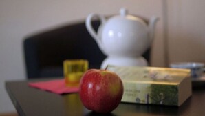 Une table avec une théière blanche, une pomme rouge et une boîte de thé.