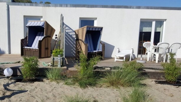 Une propriété située en bord de mer, dotée d’une terrasse en bois, de chaises longues et d’un petit jardin.