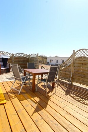 Une terrasse en bois avec une table et des chaises, entourée d’une clôture en treillis de bois.