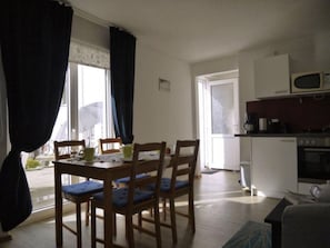 A dining area with a table and chairs, a kitchen with appliances, and a door leading outside.
