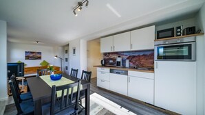 A modern kitchen with white cabinets, a dining table with chairs, a microwave, and an oven.