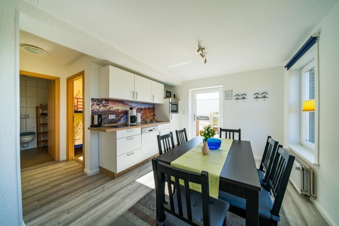 A modern kitchen with white cabinets, a dining table with chairs, and a view of the adjacent bathroom.