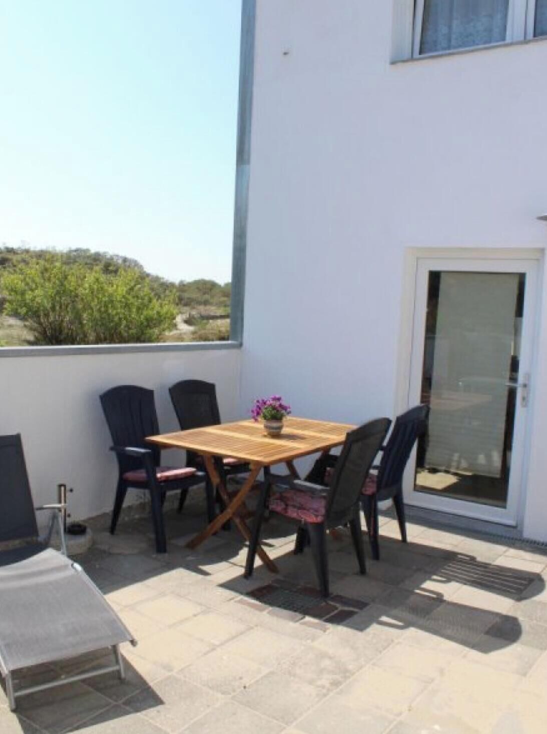 Eine Terrasse mit Holztisch und -stühlen, einem kleinen Topfpflanzen und einer Schiebetür.