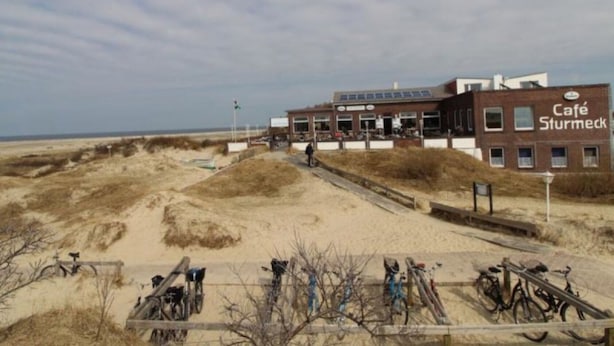A building with a sign reading 'Café Sturmeck' on a sandy beach with bicycles parked in front.
