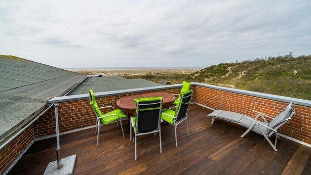 Eine Dachterrasse mit Ziegelmauer, einem runden Tisch mit Stühlen und einem Liegestuhl.
