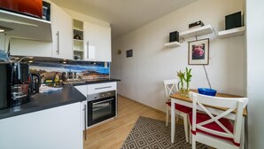 Een compacte keuken met witte kastjes, een koffieapparaat en een magnetron. Er is een eethoek met een tafel, stoelen en een klein vloerkleed.