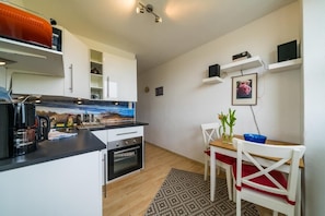 Une cuisine compacte avec des meubles blancs, une machine à café et un four à micro-ondes. On y trouve également un coin repas avec une table, des chaises et un petit tapis.