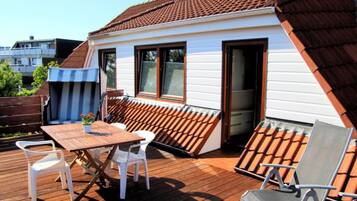 Une terrasse en bois avec une table et des chaises, un petit jardin et un bâtiment doté d’un toit en tuiles.