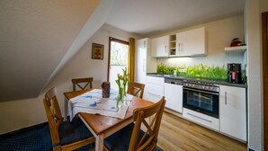A small kitchen with white cabinets, a stove, and a dining table with chairs. - Apartment 'Olde Toornblick' with Balcony and Wi-Fi (Borkum)