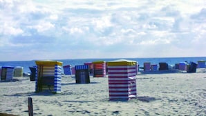 Guarda-sóis e cadeiras numa praia arenosa, com o oceano ao fundo.