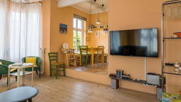 Uma sala de estar com TV, área de jantar e uma pequena mesa com cadeiras.