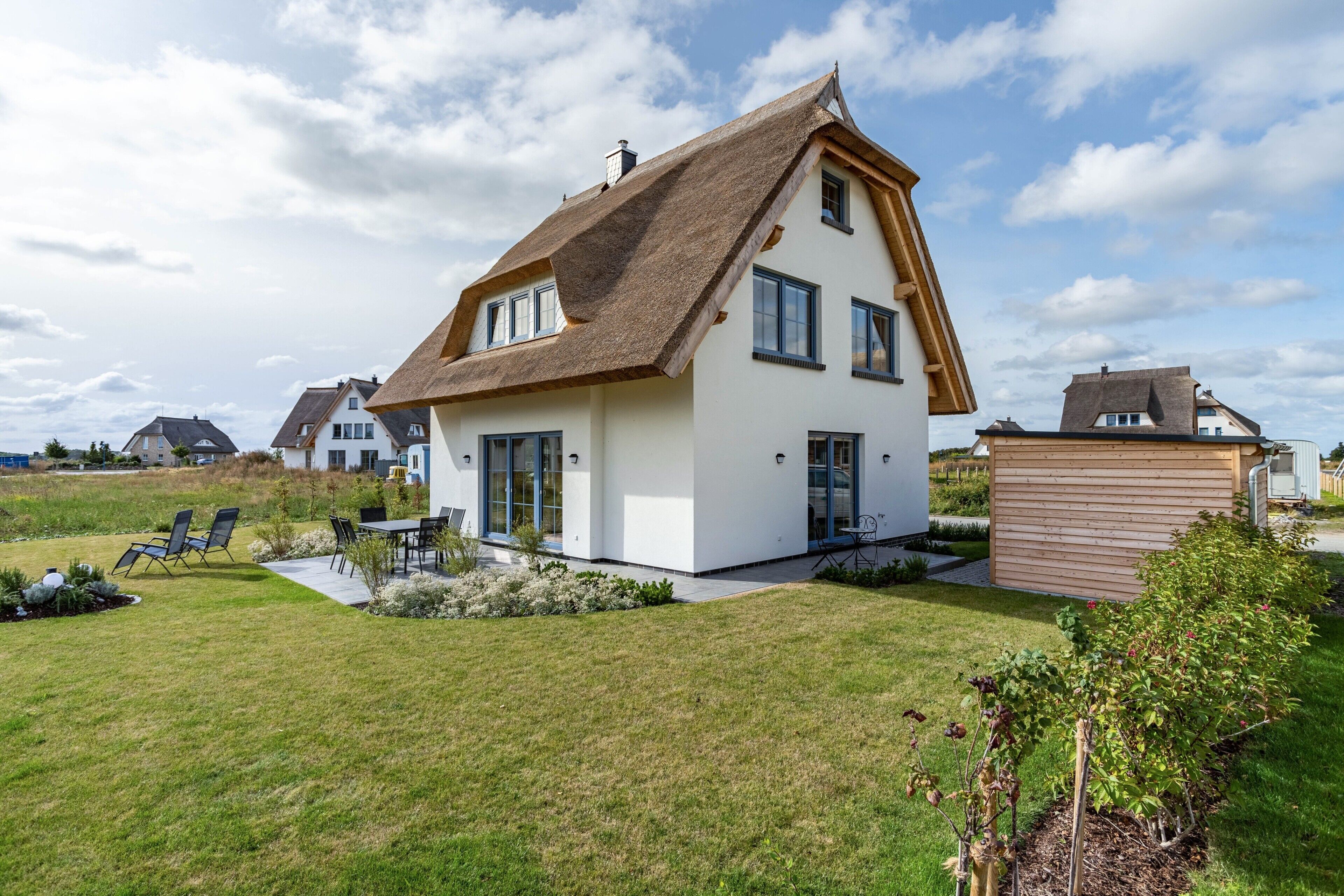 A modern house with a sloped roof, a patio with chairs, and a well-maintained lawn.